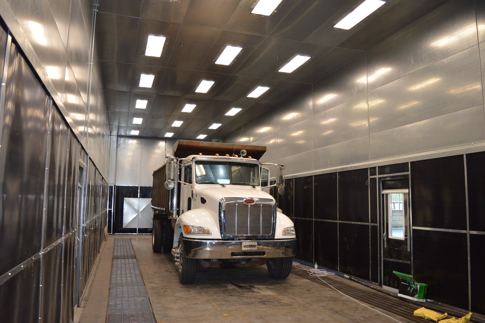 Full-size dump truck parked inside a Kresco drive-in blast room with rubber-lined walls and floor media recovery grating