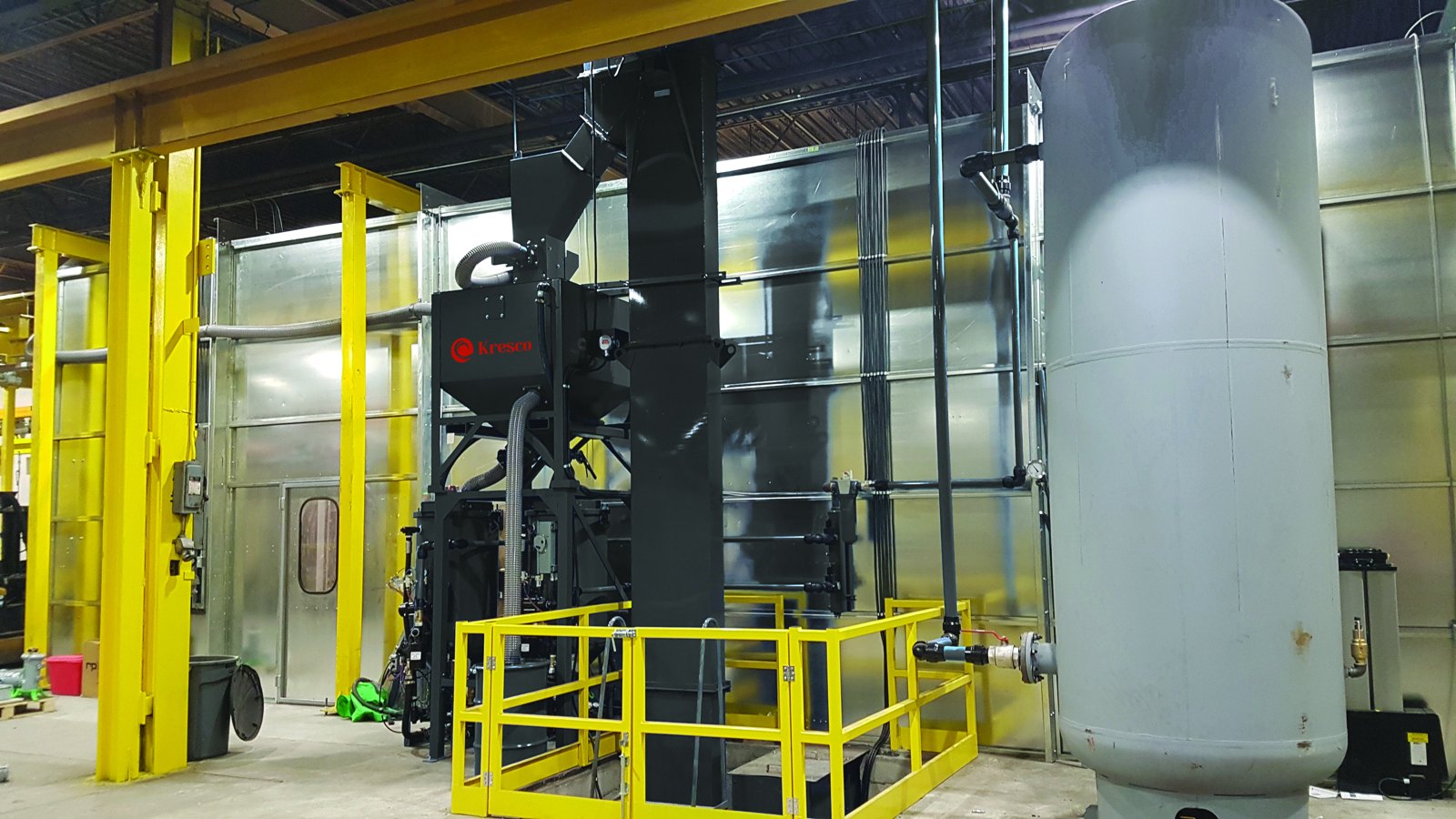 Kresco pneumatic abrasive media recovery system installed beside a blast room: bucket elevator, media classifier and storage hopper, blast pot with safety railing, and air receiver tank