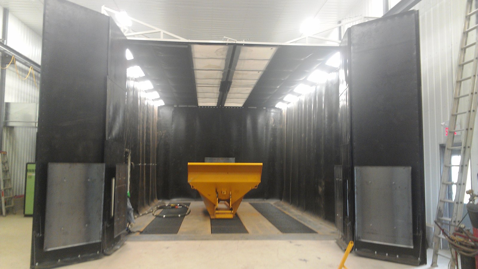 Kresco blast room with full-width doors open, hopper positioned on the grated media recovery floor ready for abrasive blasting